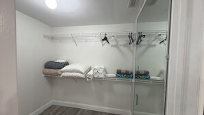 Um closet amplo com porta espelhada, prateleiras com roupas dobradas e uma luminária no teto.