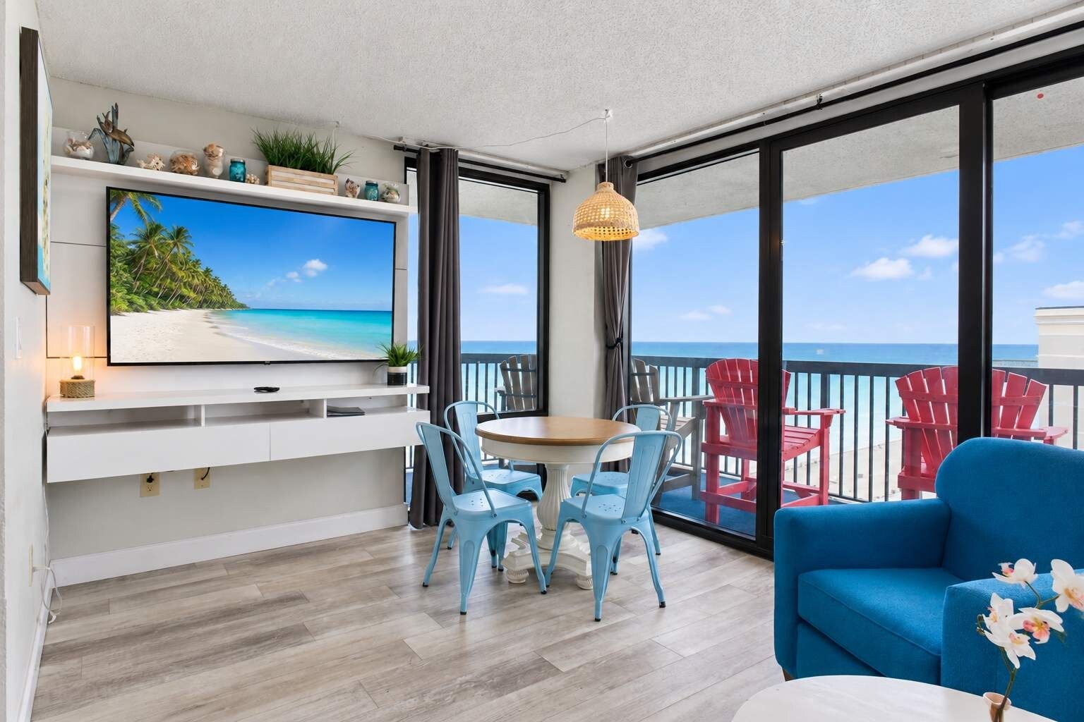 A balcony with a dining area, a TV mounted on the wall, and a view of the ocean.