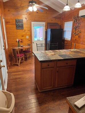 Ein Holzinterieur mit Kücheninsel, Esstisch, Stühlen und einem Kühlschrank.