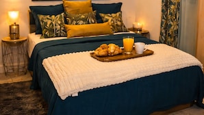 Un dormitorio con cama, almohadas, una bandeja con cruasanes y jugo, y un cuadro en la pared.