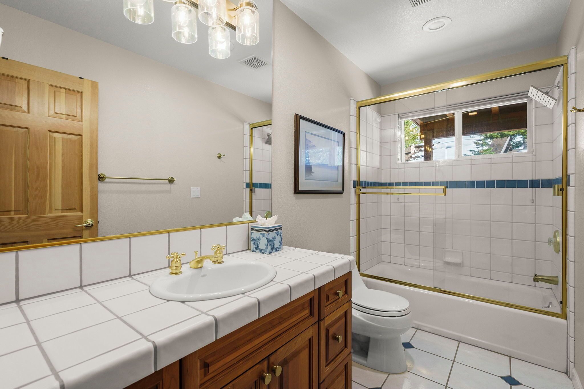 A bathroom with a white sink, gold faucets, a wooden vanity, a toilet, and a glass-enclosed shower.