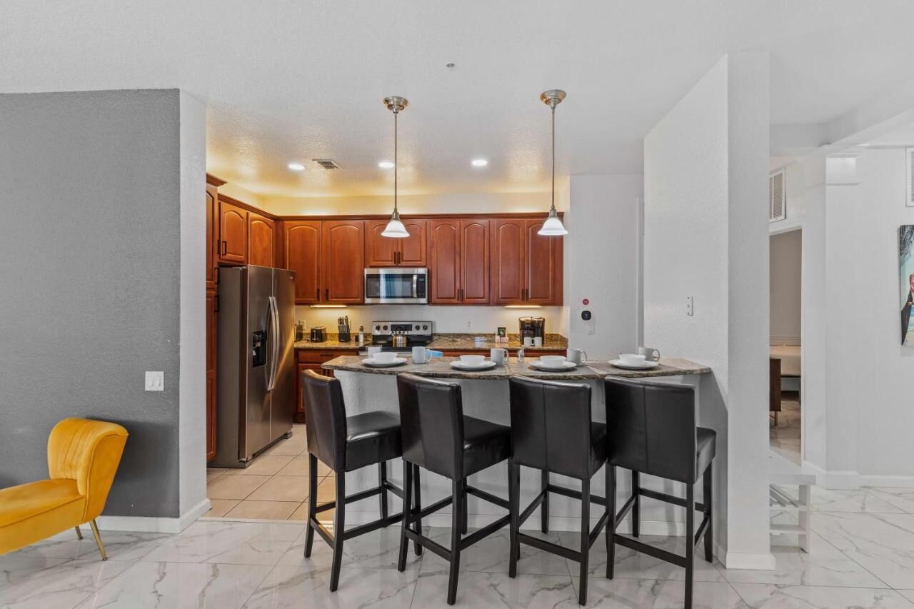 A modern kitchen with wooden cabinets, stainless steel appliances, and a bar area with black chairs.