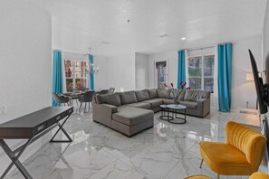 A modern living room with a sectional sofa, a small round table, a yellow armchair, and a dining area with a table and chairs. - 4840-107 Modern 4Bed Condo minutes to Theme Parks (Orlando)