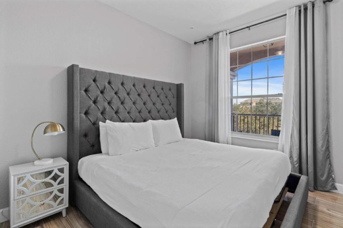 A modern bedroom with a tufted headboard, a white bedspread, and a nightstand with a lamp.