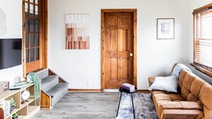 A living room with a wooden door, a sofa, a coffee table, and a TV on the left.