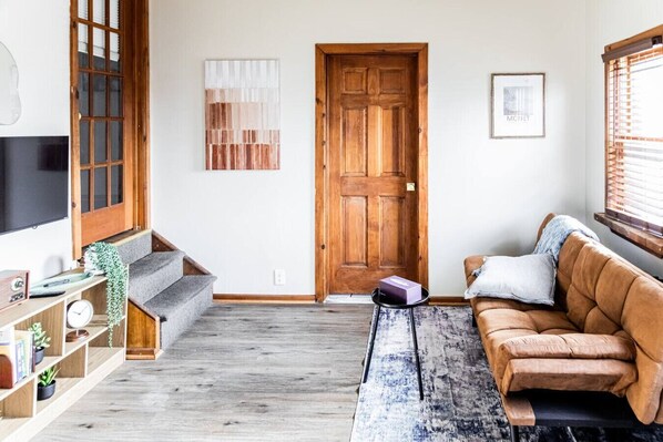 Un salon avec une porte en bois, un canapé, une table basse et un téléviseur sur le côté gauche.