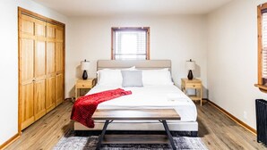 A bedroom with a bed, two bedside tables, a window, and a wooden wardrobe.