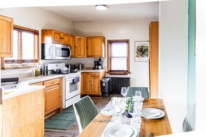 A compact kitchen with wooden cabinets, a microwave, stove, and a dining area set for four. - Charming 2BR Near NYC, MetLife & Hackensack Hosp. (Hackensack)