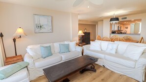 Ein geräumiges Wohnzimmer mit weißen Sofas, einem dunklen Holztisch und einem Deckenventilator.