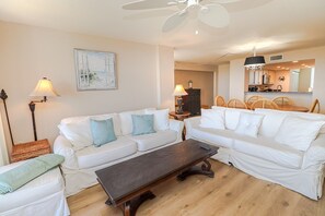 A spacious living room with white sofas, a dark wooden coffee table, and a ceiling fan. - Barefoot 211 Direct Oceanfront 2/2 (St. Augustine)