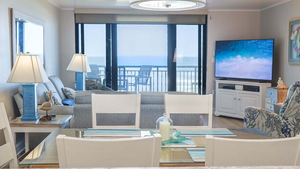 A hotel room with a balcony, a television, a dining table with chairs, and a sofa. - Barefoot Trace 409 Direct Oceanfront with Private Balcony Overlooking St. Augustine Beach (St. Augustine)