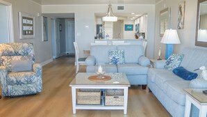A living room with a sofa, armchair, coffee table, and a dining area with a table and chairs. - Barefoot Trace 409 Direct Oceanfront with Private Balcony Overlooking St. Augustine Beach (St. Augustine)