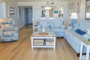 A living room with a sofa, armchair, coffee table, and a dining area with a table and chairs. - Barefoot Trace 409 Direct Oceanfront with Private Balcony Overlooking St. Augustine Beach (St. Augustine)