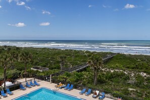 A pool with blue lounge chairs, a wooden deck, and a view of the ocean. - Barefoot Trace 409 Direct Oceanfront with Private Balcony Overlooking St. Augustine Beach (St. Augustine)