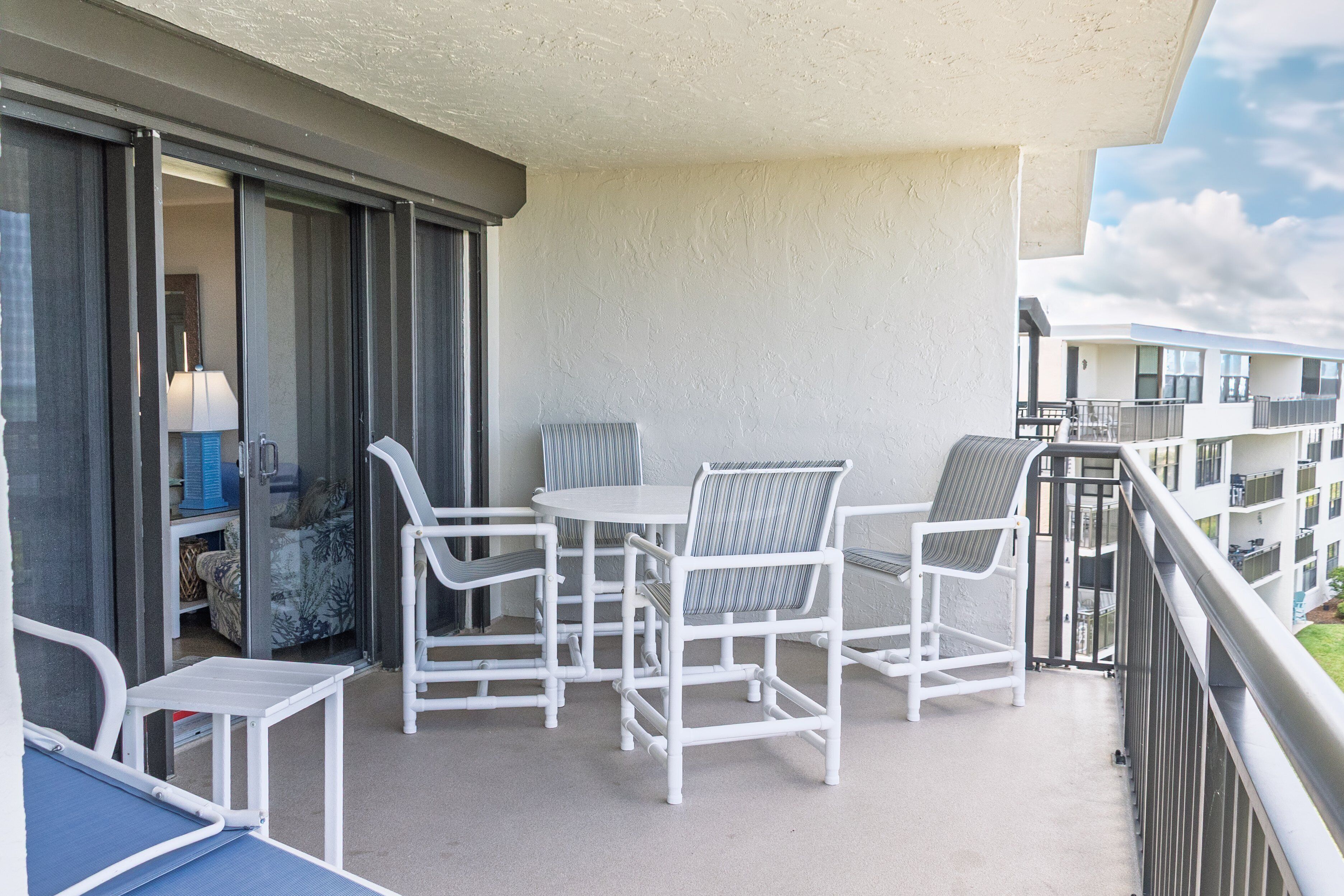 Un balcon avec une table et des chaises, une porte coulissante et une vue sur d’autres immeubles.