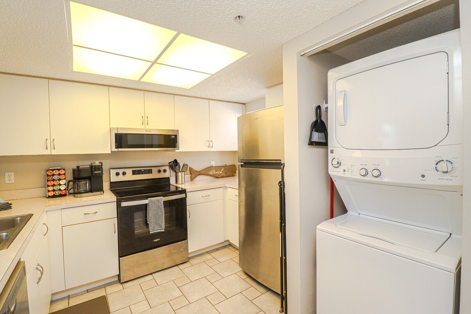 A compact kitchen with white cabinets, a stainless steel refrigerator, a microwave, an oven, and a washing machine.