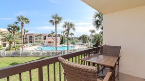 Ein Balkon mit Korbmöbeln, der einen Pool mit Palmen und ein Gebäudeensemble überblickt.