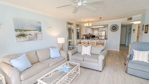 Ein Wohnzimmer mit einem beigen Sofa, einem Glastisch und einem Deckenventilator.
