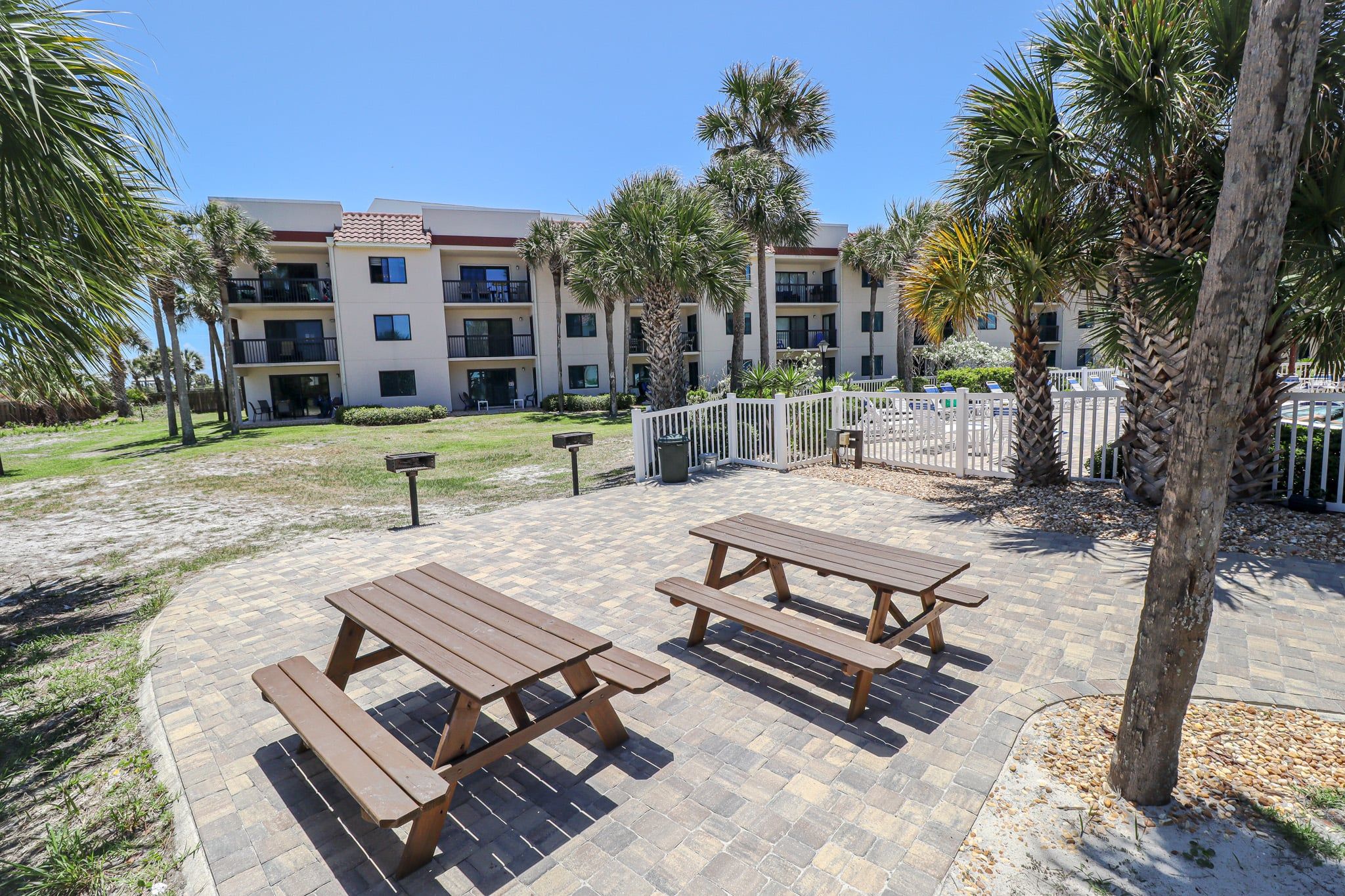 A courtyard with picnic tables and palm trees, surrounded by a building with multiple balconies.