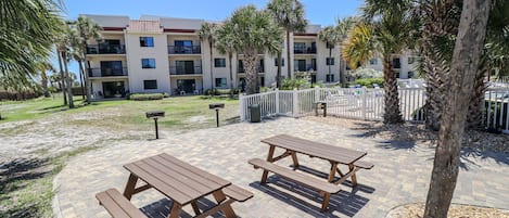 A courtyard with picnic tables and palm trees, surrounded by a building with multiple balconies.