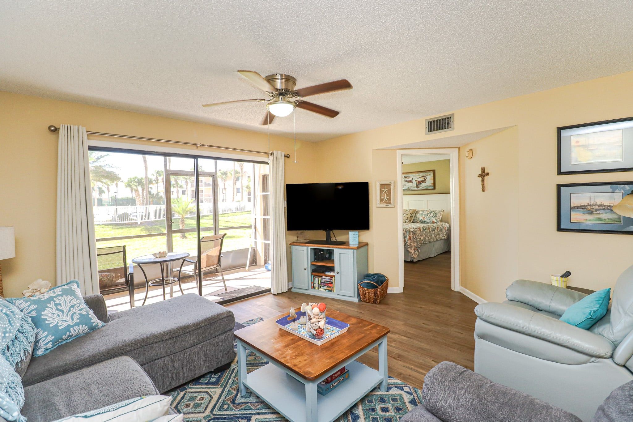 A living room with a sofa, a coffee table, a television, and a view of a balcony.