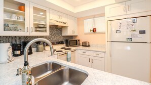 Eine moderne Küche mit weißen Schränken, einer Edelstahl-Spüle, einer Mikrowelle, einem Toaster und einem Kühlschrank.
