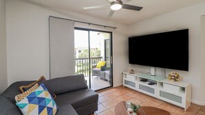 Een woonkamer met een bank, een televisie, een plafondventilator en een schuifdeur naar een balkon.
