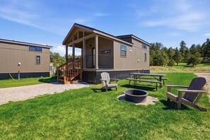 Ein zweistöckiges Gebäude mit überdachter Veranda, Sitzgelegenheiten im Freien und einem Feuerkorb.