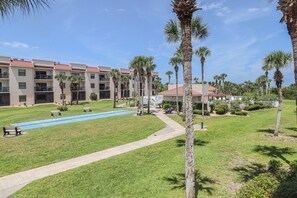 A courtyard with a swimming pool, palm trees, and a multi-story building with balconies. - Ocean Village Club O21 (St. Augustine)