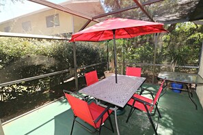 Eine überdachte Terrasse mit Tisch und Stühlen, einem roten Sonnenschirm und Blick auf ein Gewässer.