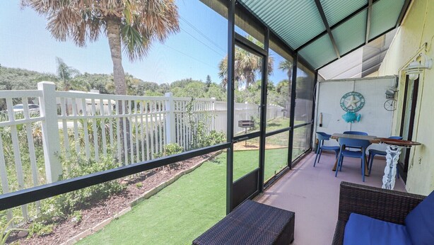A covered outdoor area with a view of a white fence and greenery, a table with chairs, and a wicker sofa. - St Augustine Beach & Tennis Resort 611-Pet-Friendly Townhome! (St. Augustine)