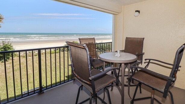 Un balcone con vista sulla spiaggia, con un tavolo rotondo e quattro sedie.