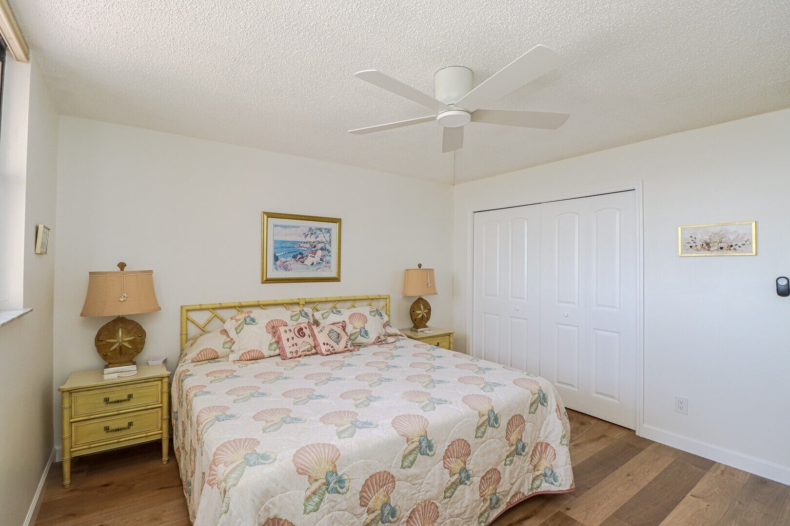 A bedroom with a bed, two bedside tables, a ceiling fan, a door, and a framed picture on the wall.