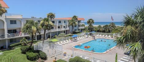 A hotel with a swimming pool surrounded by palm trees and lounge chairs.