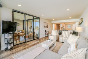 A modern living room with a sofa, armchairs, a coffee table, and a TV. There is a sliding glass door leading to a balcony. - Anastasia Condos 311-Ocean View two bedroom condo with private balcony! (St. Augustine)