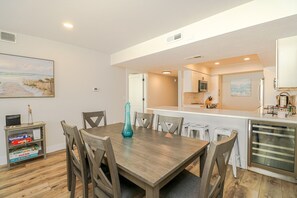 A dining area with a wooden table and chairs, a kitchen with a microwave and sink, and a small refrigerator. - Anastasia Condos 311-Ocean View two bedroom condo with private balcony! (St. Augustine)
