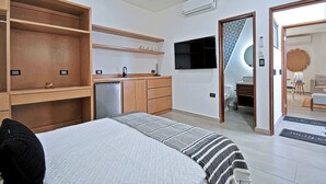 Quarto de hotel moderno com cama, cozinha compacta, banheiro e área de estar.