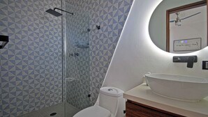 Um banheiro com parede estampada em padrão geométrico, box de vidro, vaso sanitário branco e espelho redondo com moldura e imagem.