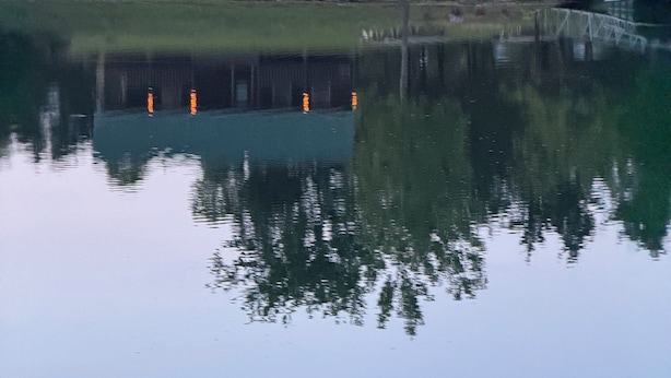 Una cabana amb un porxo, un moll i un reflex a l'aigua.