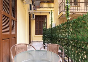 A glass table with wicker chairs in a courtyard with a yellow wall, wooden shutters, and a green hedge. - AD Neoclassical Boutique 2BR Apartment (Thessaloniki)
