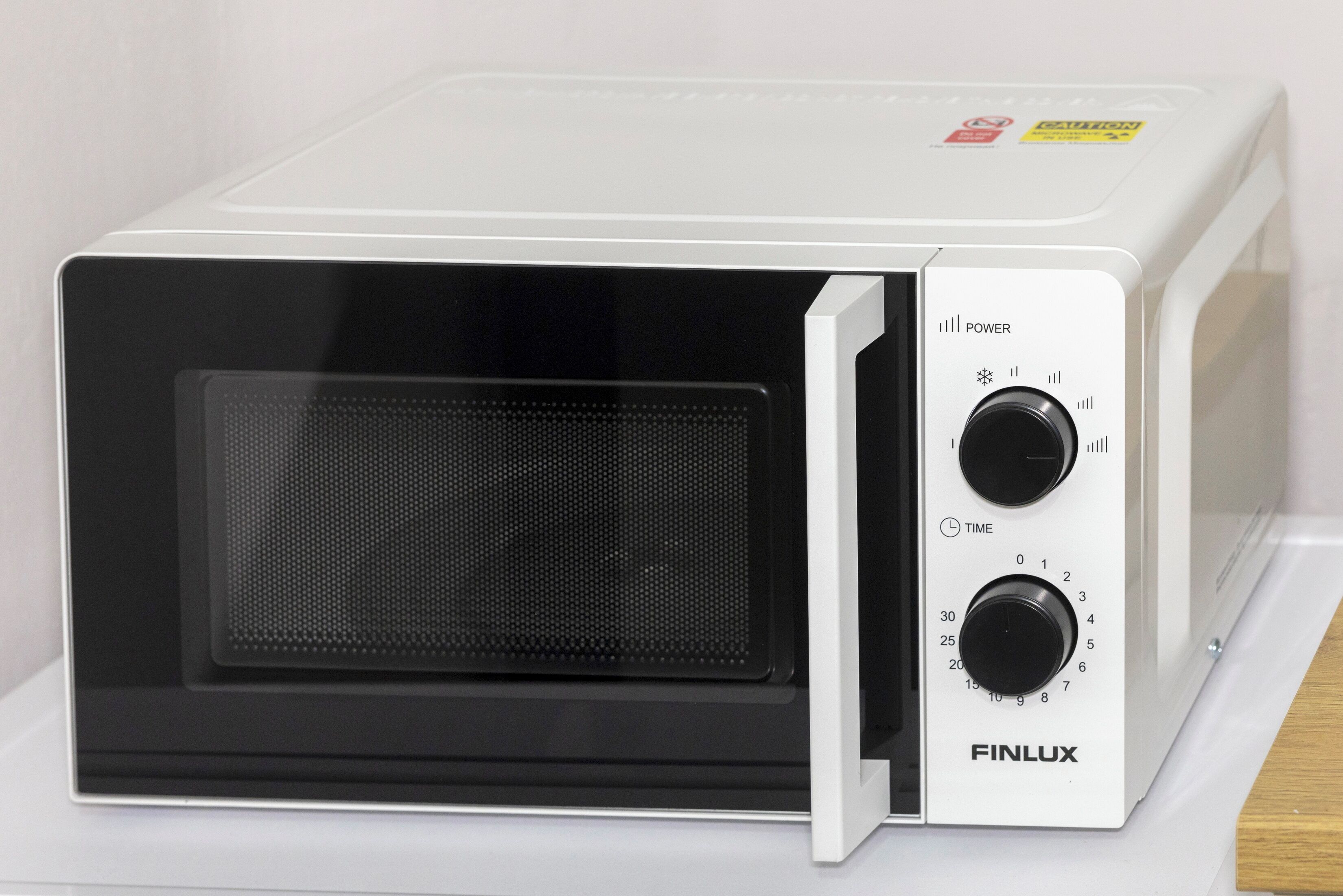 Un four à micro-ondes blanc, doté d’une porte noire, de deux boutons de commande portant les inscriptions « PUISSANCE » et « TEMPS », et de la marque « FINLUX ».
