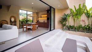 Un interior moderno con sofá, mesa de comedor y área de cocina visible a través de puertas de vidrio.