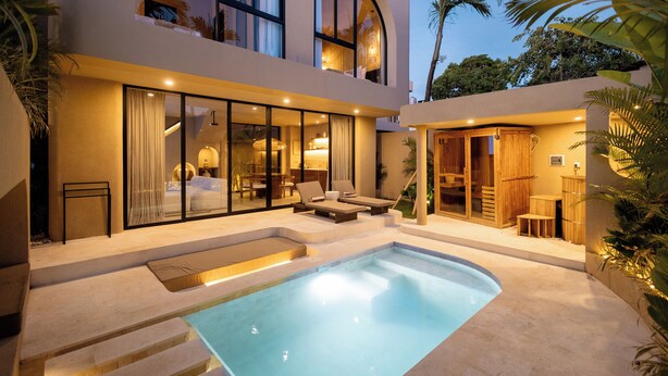 Un edificio moderno de dos plantas con piscina, mobiliario exterior y una zona cubierta con muebles de madera.