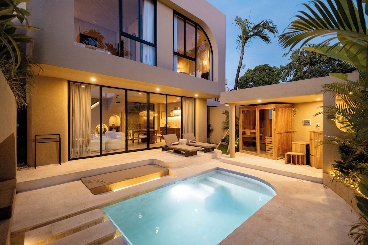 A modern two-story building with a swimming pool, outdoor seating, and a covered area with wooden furniture.