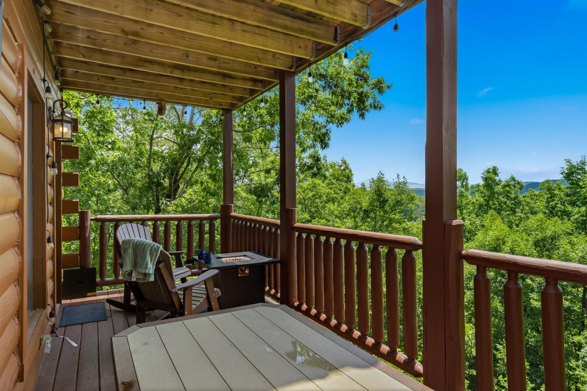 A wooden deck with a table and chairs, overlooking a forested area.