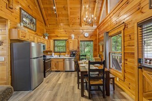 A wooden cabin interior with a kitchen, dining area, and large windows. - Epic View | Family Cabin | Hot Tub + Fire Pit | Sleeps 12 | Near Pigeon Forge (Sevierville)