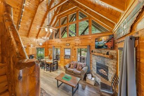 A log cabin interior with a dining area, sofa, fireplace, and large windows. - Epic View | Family Cabin | Hot Tub + Fire Pit | Sleeps 12 | Near Pigeon Forge (Sevierville)