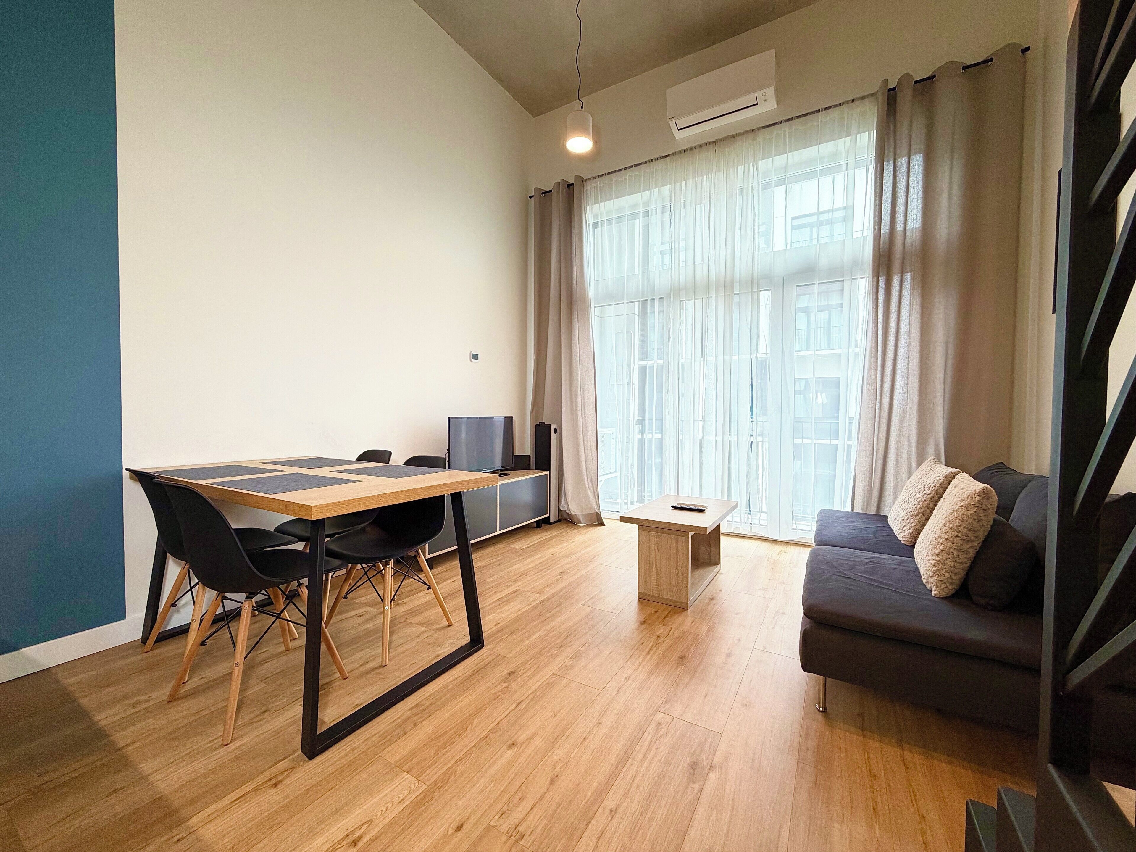 A modern living room with a wooden dining table, black chairs, a grey sofa, and a small coffee table.
