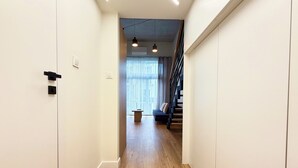 Moderni eteinen, jossa on puulattia, valkoiset seinät ja geometrisesti kuvioitu portaikko.