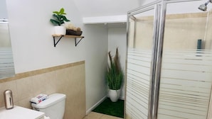 A bathroom with a toilet, sink, shower, and a shelf with plants. - Modern Quiet Suite (Newark)